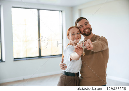 Happy couple as new owners of the house holding the keys in hands Happy couple as new owners of the house holding the keys in hands 129822558