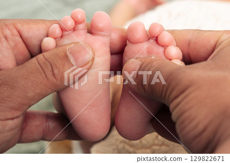 Close-up image showing adult hands gently holding and examining tiny baby feet, emphasizing tenderness and care. The interaction symbolizes love, protection, and connection. 129822671