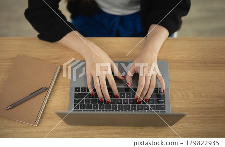 Close-Up of Hands Typing on Laptop Keyboard at Wooden Desk with Notebook and Pen Beside, Showcasing Productivity and Work Environment in Focused Setting 129822935