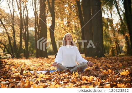 Front view. Young beautiful woman is doing yoga in the autumn park Front view. Young beautiful woman is doing yoga in the autumn park 129823212