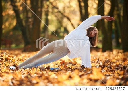 Asana for flexibility. Young beautiful woman is doing yoga in the autumn park 129823227