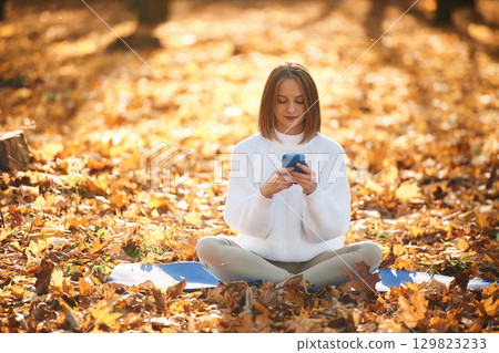 Woman is sitting in the autumn park or forest with smartphone in hands 129823233
