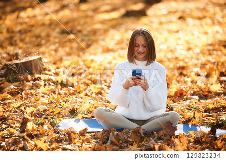 Woman is sitting in the autumn park or forest with smartphone in hands 129823234