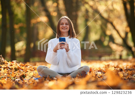 Woman is sitting in the autumn park or forest with smartphone in hands 129823236