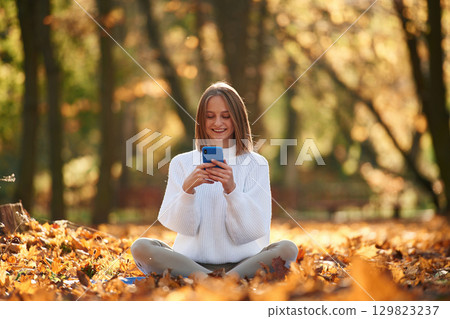 Woman is sitting in the autumn park or forest with smartphone in hands 129823237