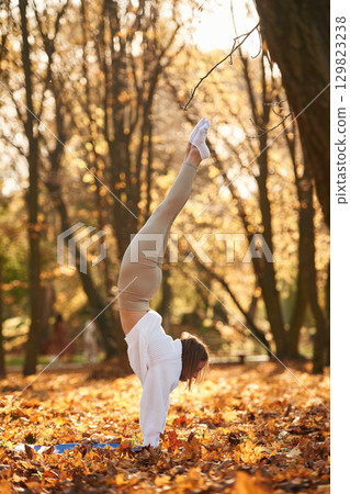 Standing on the hands. Young beautiful woman is doing yoga in the autumn park Standing on the hands. Young beautiful woman is doing yoga in the autumn park 129823238