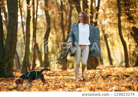 Walking together. Woman is with her cute dog in the autumn forest Walking together. Woman is with her cute dog in the autumn forest 129823274