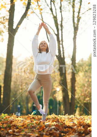 Illuminated by sunlight. Young beautiful woman is doing yoga in the autumn park 129823288