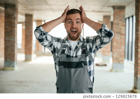 Surprised and shocked. Construction worker in uniform in empty unfinished room Surprised and shocked. Construction worker in uniform in empty unfinished room 129823678