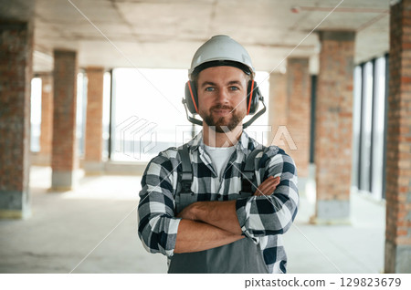 Portrait, in hard hat. Construction worker in uniform in empty unfinished room Portrait, in hard hat. Construction worker in uniform in empty unfinished room 129823679