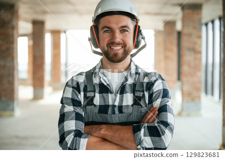 Portrait, in hard hat. Construction worker in uniform in empty unfinished room Portrait, in hard hat. Construction worker in uniform in empty unfinished room 129823681