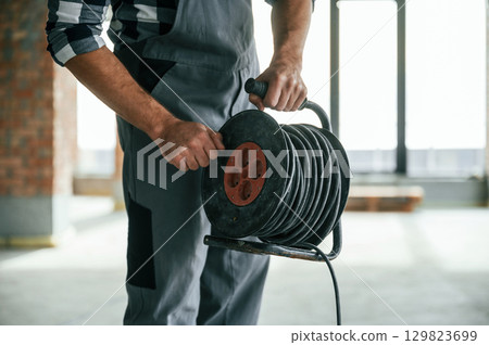 Holding wires. Close up view of repairman indoors in unfinished building Holding wires. Close up view of repairman indoors in unfinished building 129823699