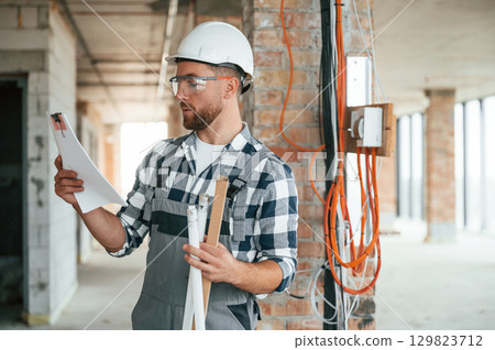 Planning the project, with paper. Construction worker in uniform in empty unfinished room 129823712