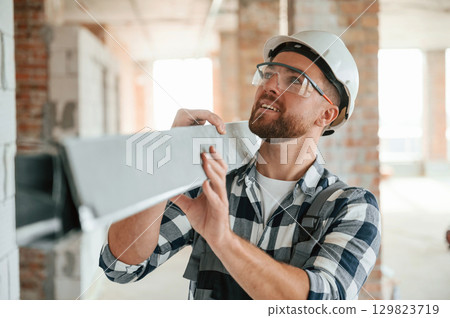 With metal plank in hands. Construction worker in uniform in empty unfinished room 129823719