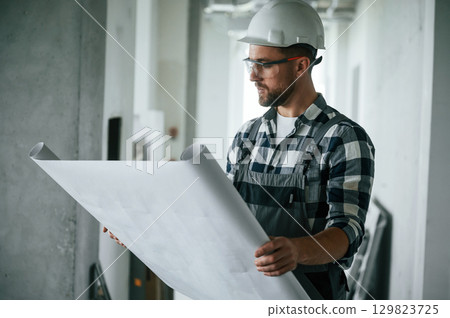 Project on the paper, holding in hands. Construction worker in uniform in empty unfinished room Project on the paper, holding in hands. Construction worker in uniform in empty unfinished room 129823725