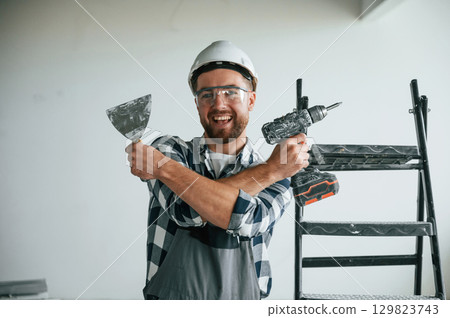 With drill. Repairman in uniform is in the unfinished building With drill. Repairman in uniform is in the unfinished building 129823743