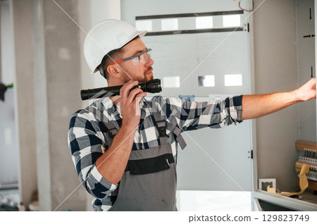 Using flashlight. Repairman in uniform is in the unfinished building Using flashlight. Repairman in uniform is in the unfinished building 129823749