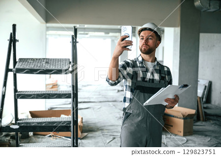 Planning the project, with paper. Construction worker in uniform in empty unfinished room 129823751