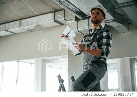Checking the ceiling. Construction worker in uniform in empty unfinished room 129823754