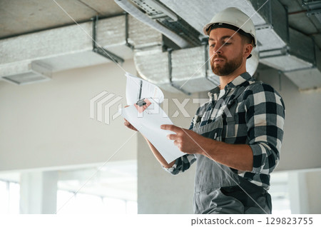 Checking the ceiling. Construction worker in uniform in empty unfinished room Checking the ceiling. Construction worker in uniform in empty unfinished room 129823755