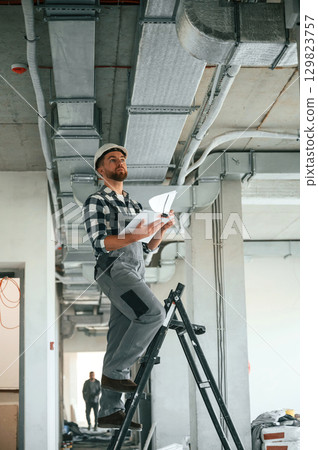 Checking the ceiling. Construction worker in uniform in empty unfinished room Checking the ceiling. Construction worker in uniform in empty unfinished room 129823757