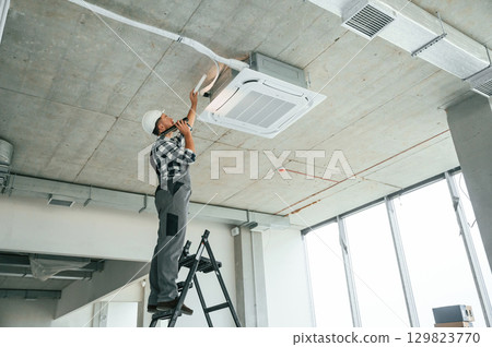 Fixing ventilation system. Repairman in uniform is in the unfinished building Fixing ventilation system. Repairman in uniform is in the unfinished building 129823770