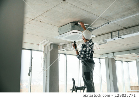 Fixing ventilation system. Repairman in uniform is in the unfinished building Fixing ventilation system. Repairman in uniform is in the unfinished building 129823771