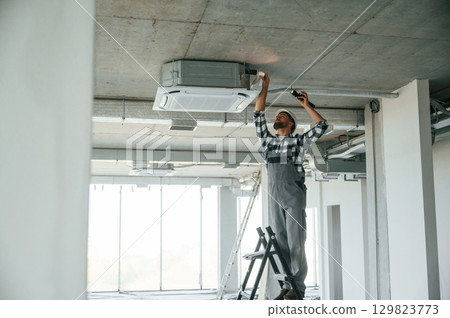 Setting the ventilation system. Repairman in uniform is in the unfinished building Setting the ventilation system. Repairman in uniform is in the unfinished building 129823773