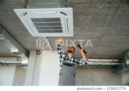 Using flashlight. Repairman in uniform is in the unfinished building Using flashlight. Repairman in uniform is in the unfinished building 129823774