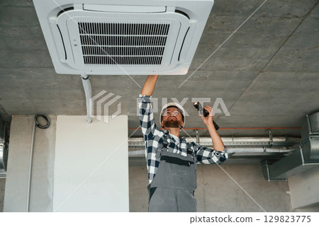 Using flashlight. Repairman in uniform is in the unfinished building 129823775