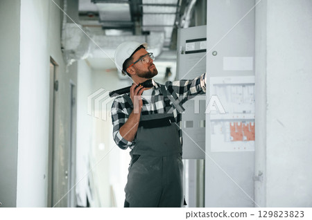 Side view, using flashlight, checking the electricity box. Repairman in uniform is in the unfinished building 129823823