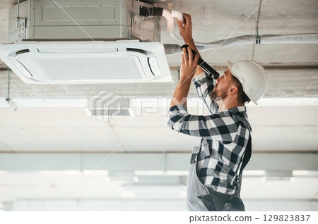 Setting up the ventilation system on the ceiling. Repairman in uniform is in the unfinished building Setting up the ventilation system on the ceiling. Repairman in uniform is in the unfinished building 129823837