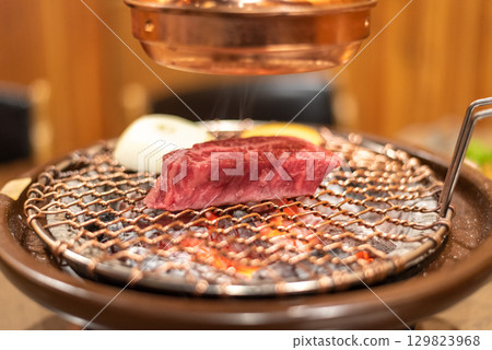 A piece of raw meat grilling on a Korean charcoal barbecue 129823968