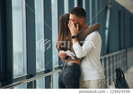 Man is crying, embracing, farewell. Couple are in the airport hall together Man is crying, embracing, farewell. Couple are in the airport hall together 129824599