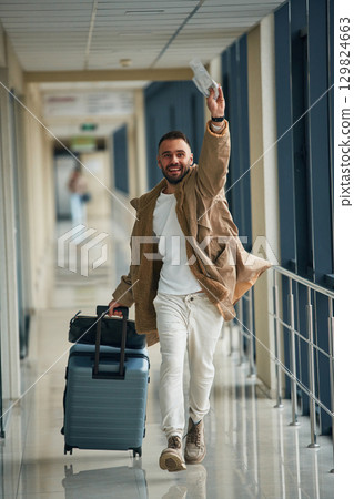 Running, late for flight, with tickets in hand. Young handsome man in the airport Running, late for flight, with tickets in hand. Young handsome man in the airport 129824663
