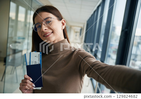 Smiling, holding tickets. Young woman traveler in the airport entrance hall Smiling, holding tickets. Young woman traveler in the airport entrance hall 129824682