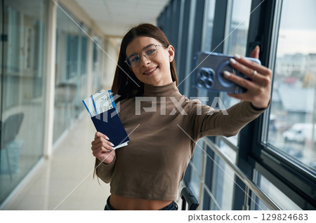Making selfie with phone, smiling. Young woman traveler in the airport entrance hall Making selfie with phone, smiling. Young woman traveler in the airport entrance hall 129824683
