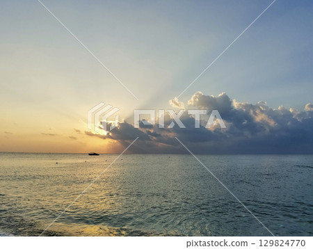 Serene ocean sunrise with vibrant clouds reflecting on calm water surface and distant boat 129824770