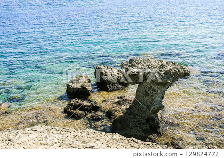 Unique rock formation stands majestically by the clear blue water of the tranquil seascape 129824772