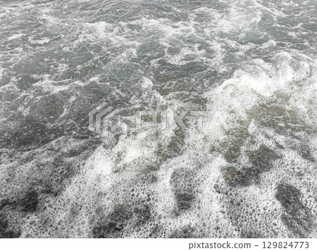 Sea waves crashing on rocky shore creating foam and ripples in a dynamic water scene 129824773