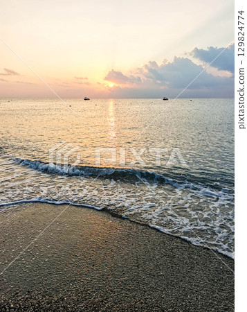 Serene beach at sunrise with gentle waves lapping against the shore and colorful sky reflections Serene beach at sunrise with gentle waves lapping against the shore and colorful sky reflections 129824774