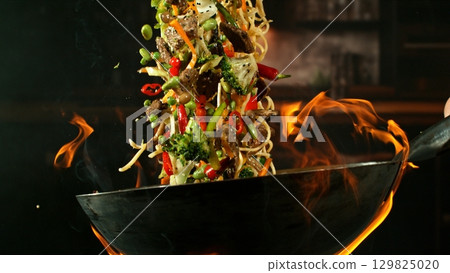 Freeze Motion of Wok Pan with Flying Ingredients in the Air and Fire Flames. Kitchen Interior on Background. Freeze Motion of Wok Pan with Flying Ingredients in the Air and Fire Flames. Kitchen Interior on Background. 129825020
