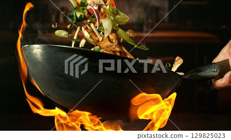 Freeze Motion of Wok Pan with Flying Ingredients in the Air and Fire Flames. Kitchen Interior on Background. 129825023
