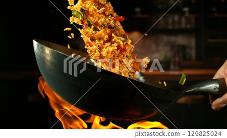 Freeze Motion of Wok Pan with Flying Spanish Paella up in the Air and Fire Flames. Kitchen Interior on Background. 129825024