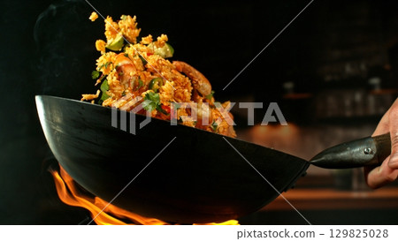 Freeze Motion of Wok Pan with Flying Spanish Paella up in the Air and Fire Flames. Kitchen Interior on Background. 129825028