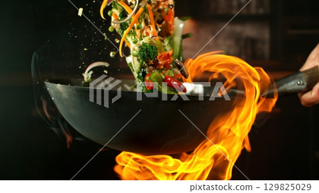 Freeze Motion of Wok Pan with Flying Ingredients in the Air and Fire Flames. Kitchen Interior on Background. Freeze Motion of Wok Pan with Flying Ingredients in the Air and Fire Flames. Kitchen Interior on Background. 129825029