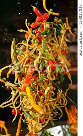 Freeze Motion of Wok Pan with Flying Ingredients in the Air and Fire Flames. Kitchen Interior on Background. Vertical Aspect Ratio. 129825038