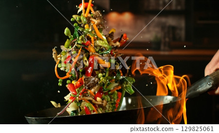 Freeze Motion of Wok Pan with Flying Ingredients in the Air and Fire Flames. Kitchen Interior on Background. Freeze Motion of Wok Pan with Flying Ingredients in the Air and Fire Flames. Kitchen Interior on Background. 129825061