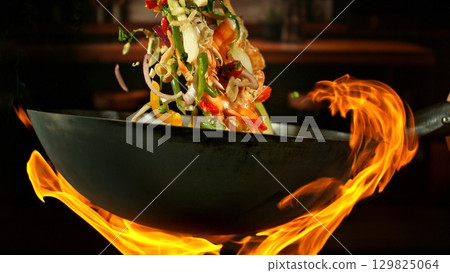 Freeze Motion of Wok Pan with Flying Ingredients in the Air and Fire Flames. Kitchen Interior on Background. 129825064