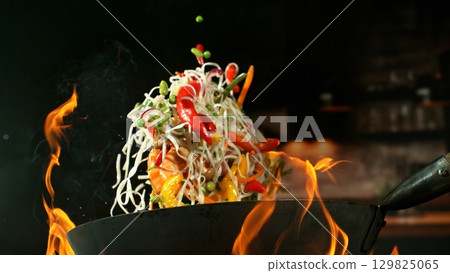 Freeze Motion of Wok Pan with Flying Ingredients in the Air and Fire Flames. Kitchen Interior on Background. 129825065